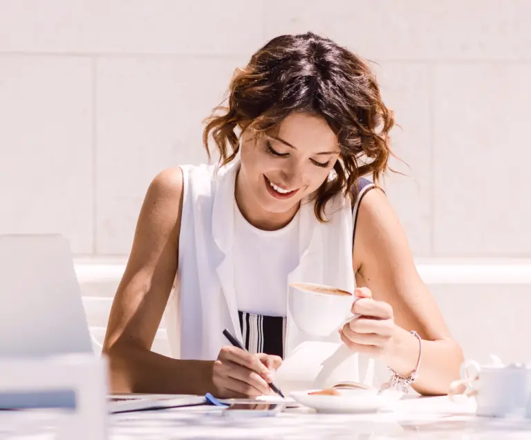 Uma mulher de roupa branca segurando uma xícara de café preenchendo um relatório